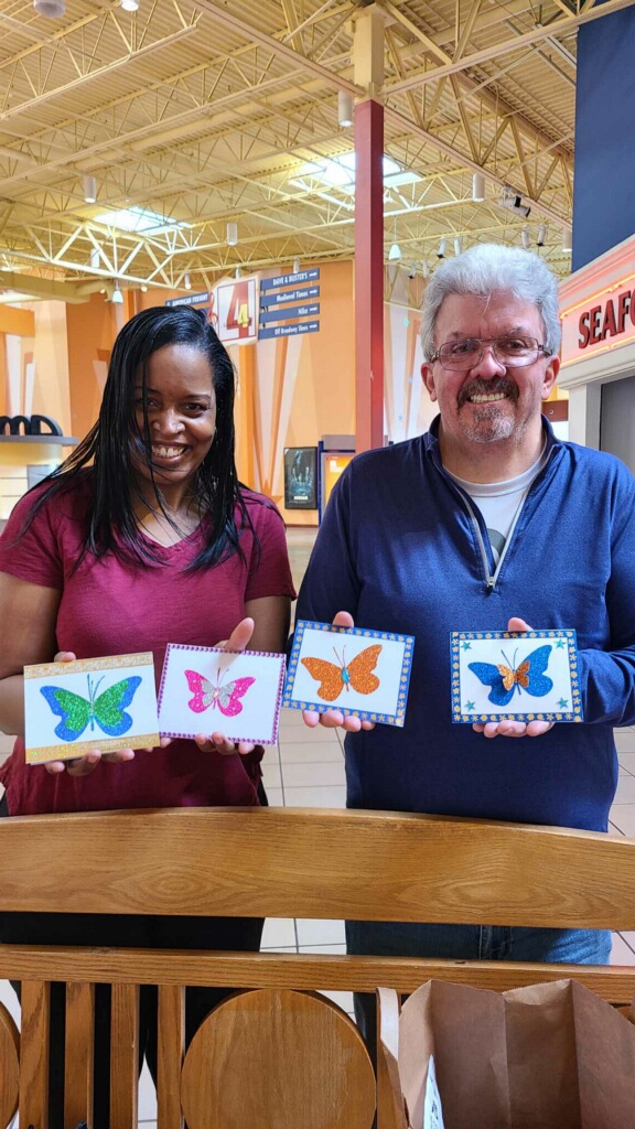 A Black woman and a white man hold up Kymberlee's encouragement cards that she makes for the brain tumor community.
