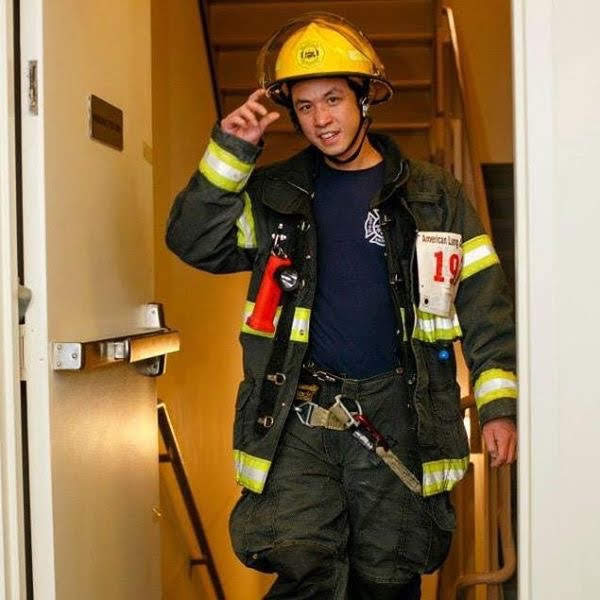 A male firefighter walks up the stairs with his hand up as if he's about to remove his yellow helmet.
