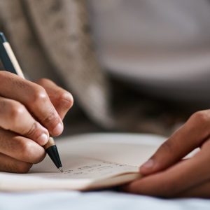 Cropped shot of a man writing in a notebook on his bed at home. Aphasia can impact one's ability to write, speak, or understand.
