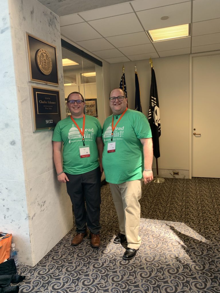 Two men in green Head to the Hill shirts stand outside a representative's office during the event.