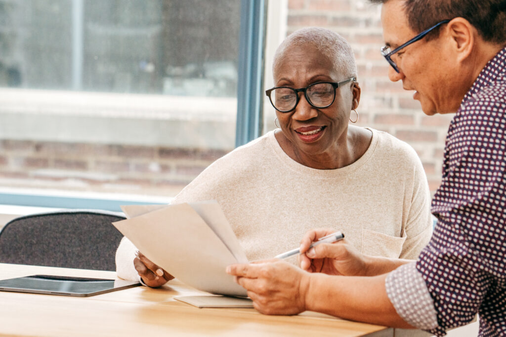 A Black woman looks at paperwork. Patient support programs may help with the expenses associated with brain tumor treatment.