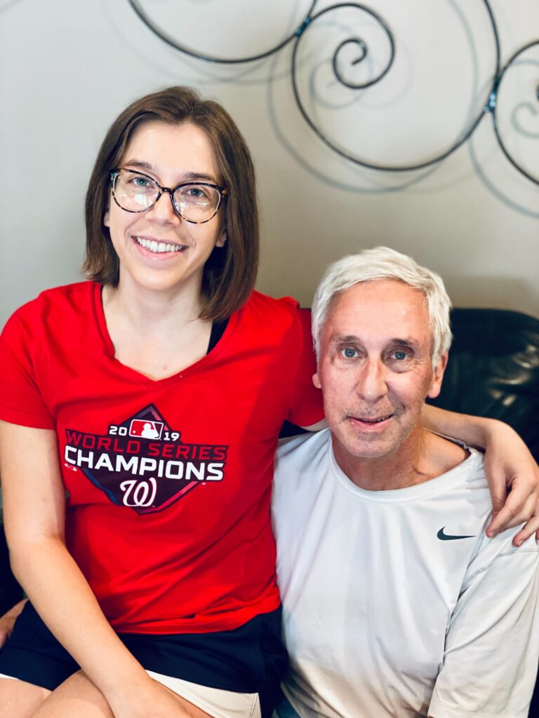 A young adult woman in glasses wears a 2019 World Series Champions t-shirt sitting next to her father.