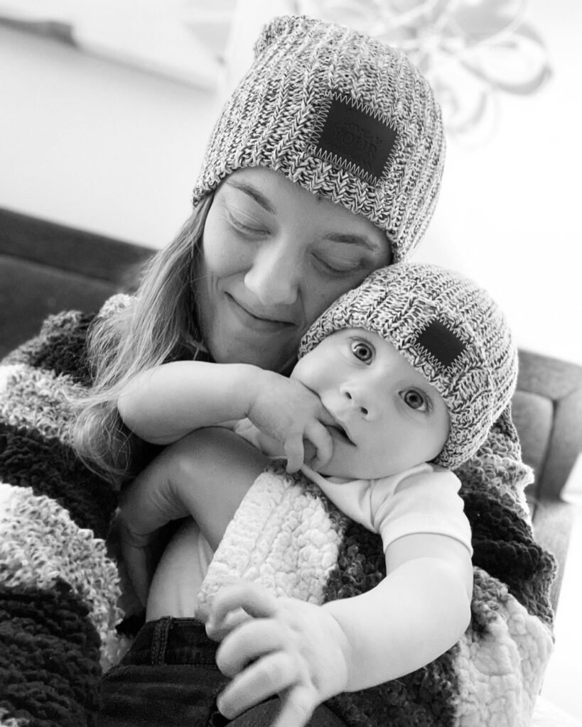 A black and white photo of a mom holding her infant — both wearing beanies.