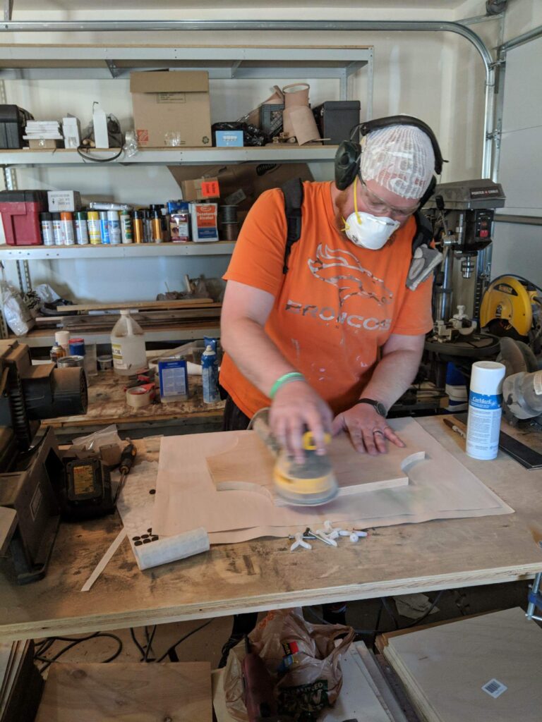 A man wearing his Optune medical device and headphones is focused on his woodworking hobby.