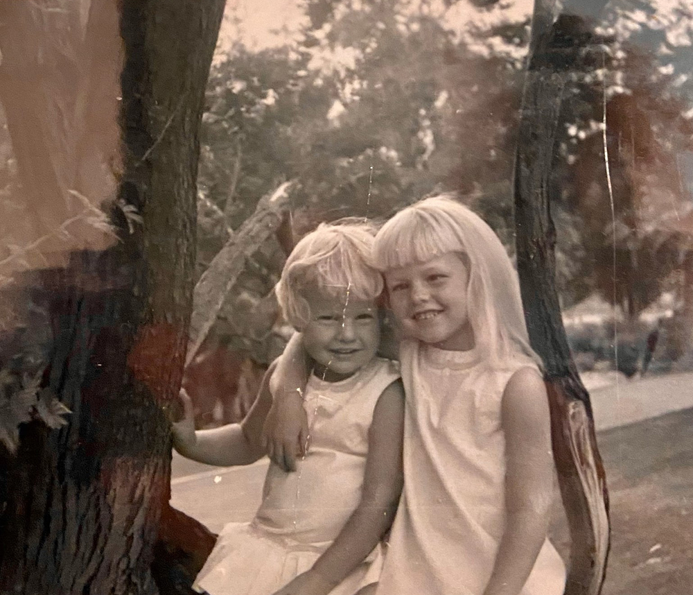 Two little girls sit on a tree in a photo from the 1970s.