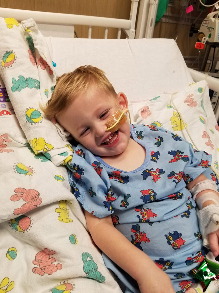 A pediatric ependymoma patient, age 2, smiles in their hospital bed.
