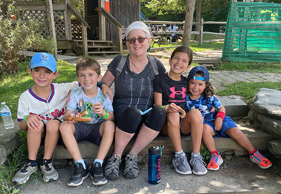 A woman, wearing an Optune medical device, joins her four grandchildren for a fun outdoor activity. She also spends time mentoring other patients.