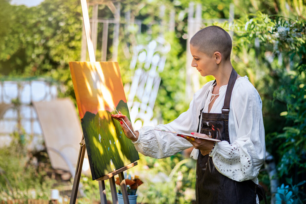 Young woman with brain cancer relaxing while painting an art canvas outdoors in her garden. 
