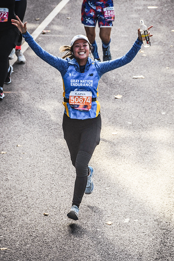 A woman runs with her hands up during a marathon in honor of her dad living with a brain tumor.