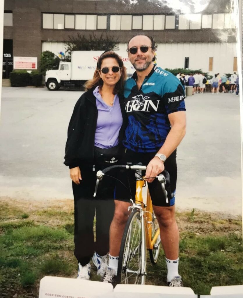 In a photo from the 1990s, a man and woman stand by a bicycle at a brain tumor research fundraiser.