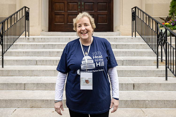 A woman stands in front of steps in D.C., wearing her navy blue Head to the Hill t-shirt.