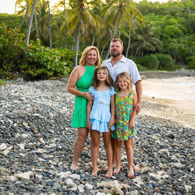 A family — a man, a woman, and two young girls — stand on a rocky beach.  Biomarker testing changed how this family makes their daily and long-term decisions.