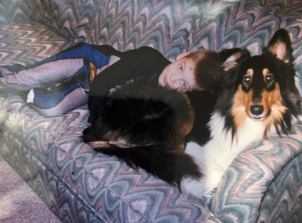 A young boy rests on his tri-color Collie while resting on the patterned couch. 