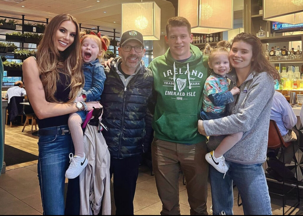 Two women holding young girls stand alongside a man in an Ireland sweatshirt and a man living with glioblastoma in a baseball hat.