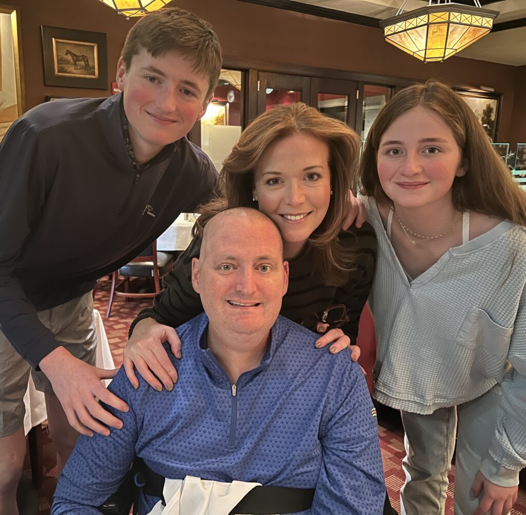 A standing woman rests her hands on her husband's shoulders, who is sitting, with their two kids — a boy and girl — on either side.