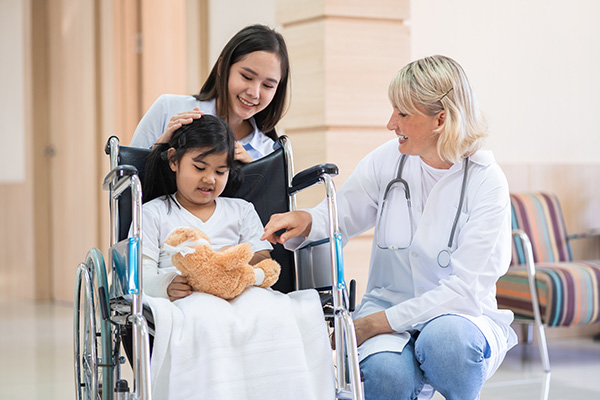 Female pediatrician doctor and child patient on wheelchair with her mother in the health medical center talk about returning to school.