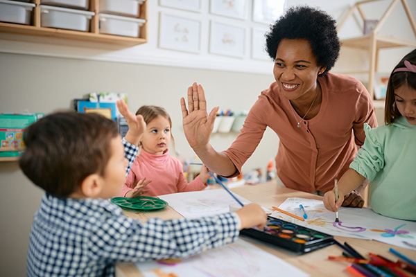 Happy African American teacher and small boy giving high-five during while kindergarteners make art for their classmate with a brain tumor.