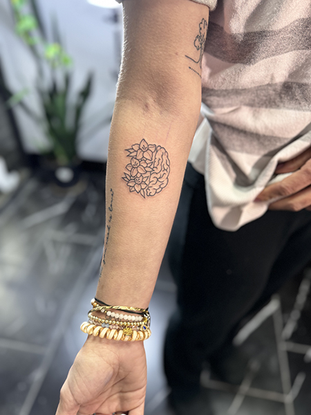 Danielle shows a few tattoos on her arm, including one that looks like a half brain on the right and flowers/leaves on the left.