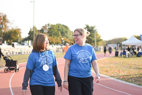 Two women in blue event t-shirts walk on a track, looking at each other and laughing.