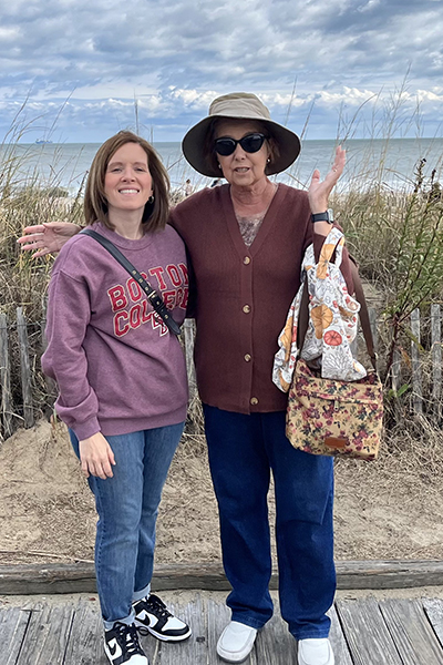 Two women, who both benefited from biomarker testing, stand on a boardwalk with the ocean behind them.