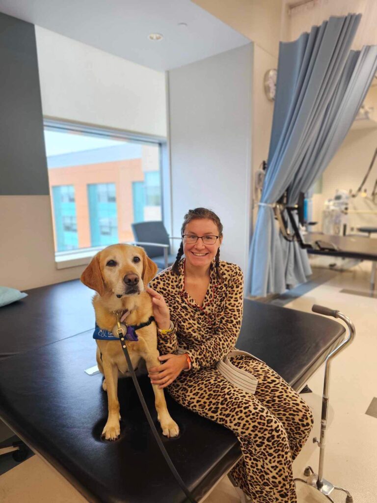 A woman sits on a therapy bed with her arms around a therapy dog.