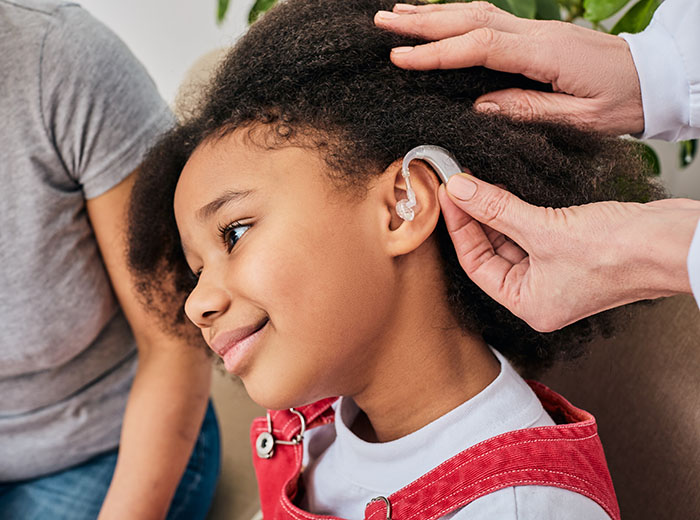 Hearing solutions for children with benign brain tumors. Doctor installs hearing aid on African American girl's ear, close-up