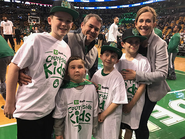 A family of four young boys, including one with DIPG, and a mom and dad stand courtside at a Boston Celtics game.