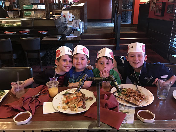 Four young boys enjoy dinner and smile for the camera.