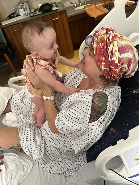 A woman in a hospital bed wearing a head scarf holds up her baby niece.