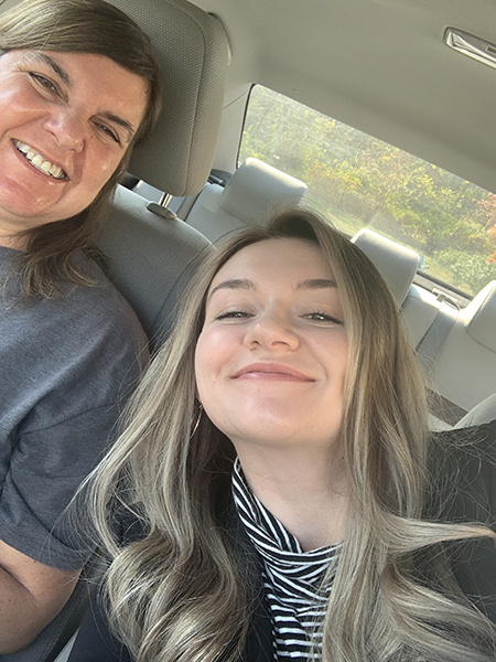 A woman with astrocytoma smiles in a car with her daughter, who leans over to smile alongside her.