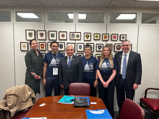 A group of brain tumor advocates, including one woman who turned to advocacy after loss, pose for a photo with Senator Jack Reed in a Senate office.