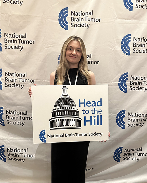 A woman in a black sleeveless dress holds up a sign that reads Head to the Hill. She turned to advocacy after loss.
