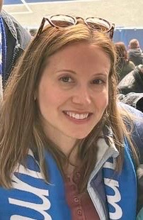 A woman smiles at the camera wearing a jacket and glasses atop her head.