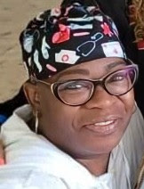 A woman smiles at the camera wearing a nurses hat, glasses, and a white shirt.