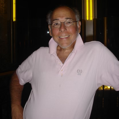 A man in a white polo leans against a counter.