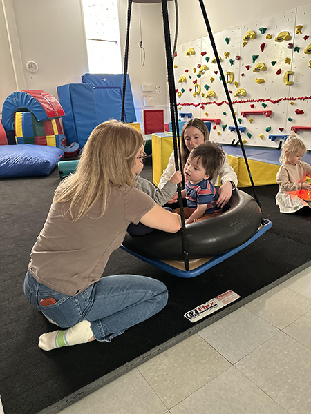 A two-year-old boy, a toddler with brain cancer, sits in a support swing during occupational therapy.