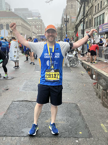 A male runner celebrates with his arms up after finishing the Boston Marathon.