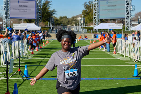 A woman celebrates, holding her arms up, after crossing the finish line of the DFW Brain Tumor Walk & Race.
