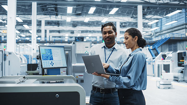 Indian male engineer and Hispanic female manager use a laptop computer at an electronics factory. 
