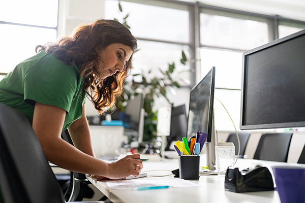 A focused professional woman working on documents at an office desk, returning to work after a brain tumor diagnosis.