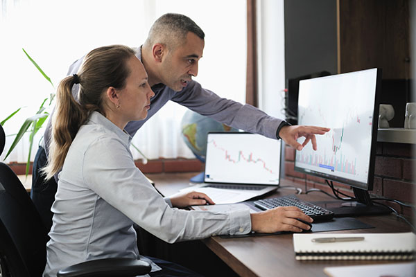 Businesspeople working in the office on stock market exchange data using desktop computer and digital tablet. One of the employees returned to the office after a brain tumor.