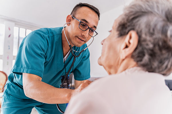 Nurse, who is returning to work after a brain tumor diagnosis, is listening to a heartbeat of a senior woman during medical consultation