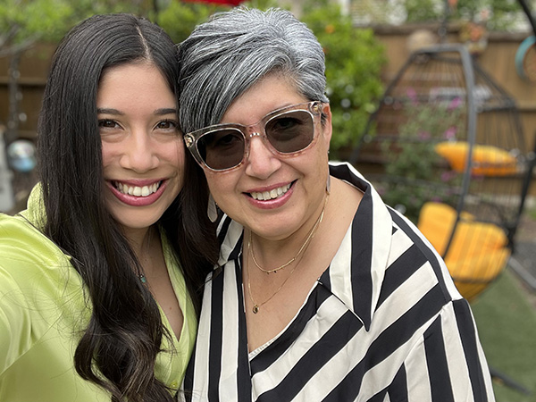 A young adult daughter in a green shirt smiles for the camera alongside her mother in a black-and-white striped shirt and sunglasses. They found community through NBTS.