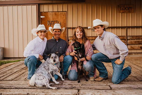 A family of four - a mom, a dad, and two young adult sons - smile for the photo. Mom holds a dog, and the three men have white cowboy hats. The mom advocates for the BRAIN Act after her husband's passing.