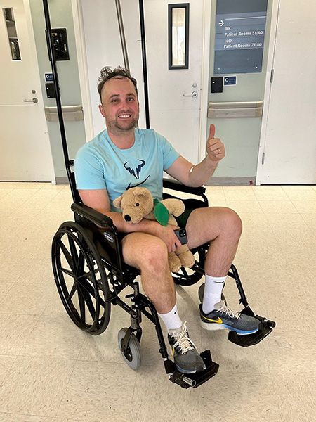 A man sits in a wheelchair, holding a stuffed animal, as he leaves the hospital following brain surgery.