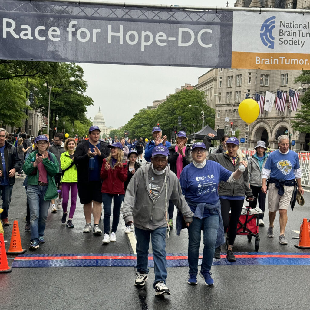 A glioblastoma survivor crosses the Race for Hope DC finish line with his wife cheering behind him.