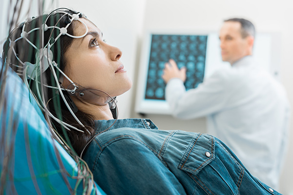 Dark-haired woman lying on an examination table and undergoing electroencephalography (EEG) for seizures while her doctor examining CT results.