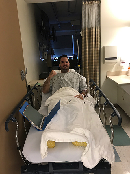 A man with meningioma sits in a hospital bed looking at the camera. It's dark outside through the window. 