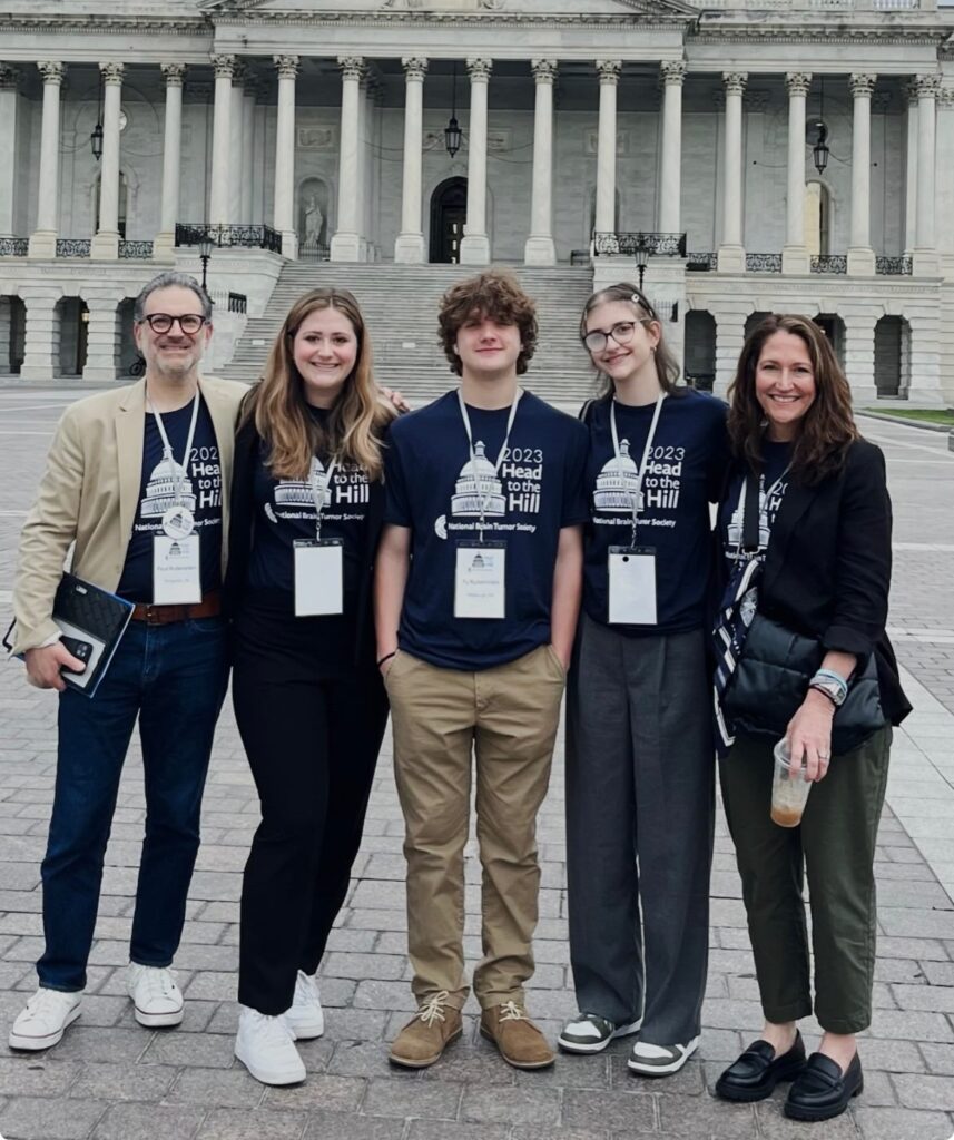 A family of five — an adult male, three young adults, and an adult female — stand in front of the Capitol at Head to the Hill before advocating for the BRAIN Act.