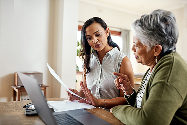 Cropped shot of a young woman, who is an oncology social worker, sitting and explaining paperwork to an elderly woman with a brain tumor.
